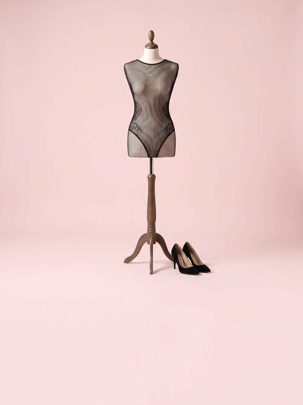 Czarny bodystocking z siatki na manekinie obok czarnych szpilek